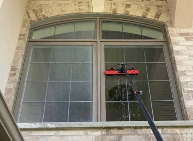 Window cleaner washing an arched window with a pole in Lathrop, CA